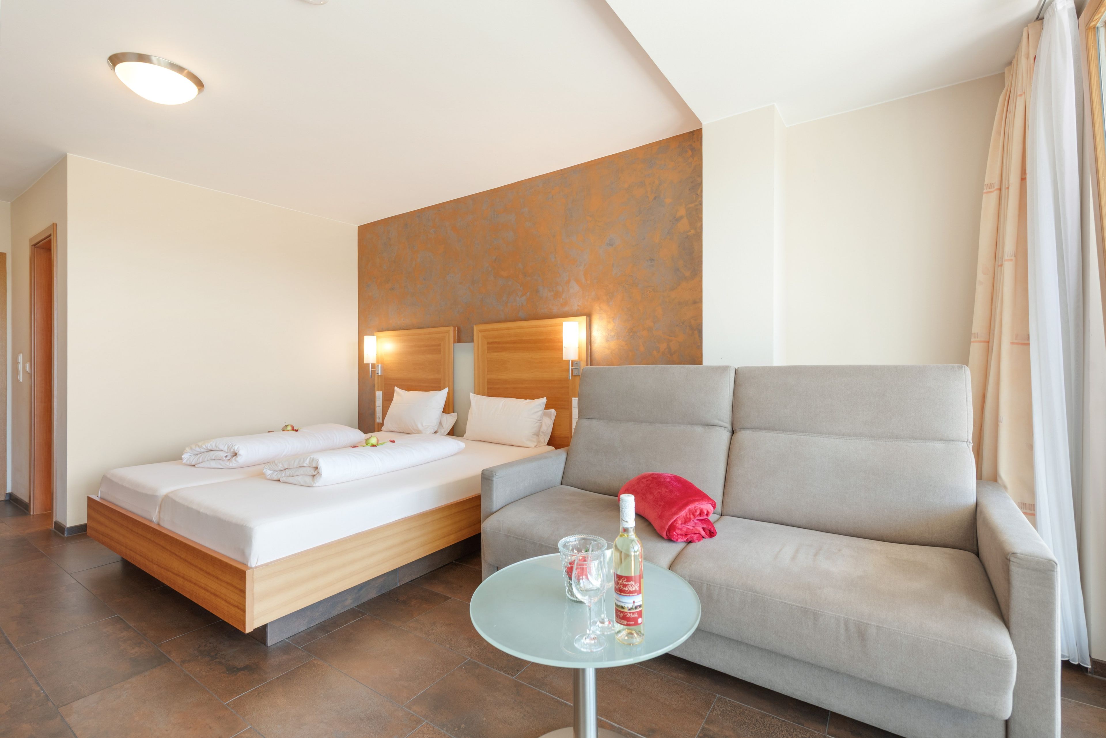 Une chambre d’hôtel avec un lit, un canapé, une petite table et un mur orné d’un motif texturé.