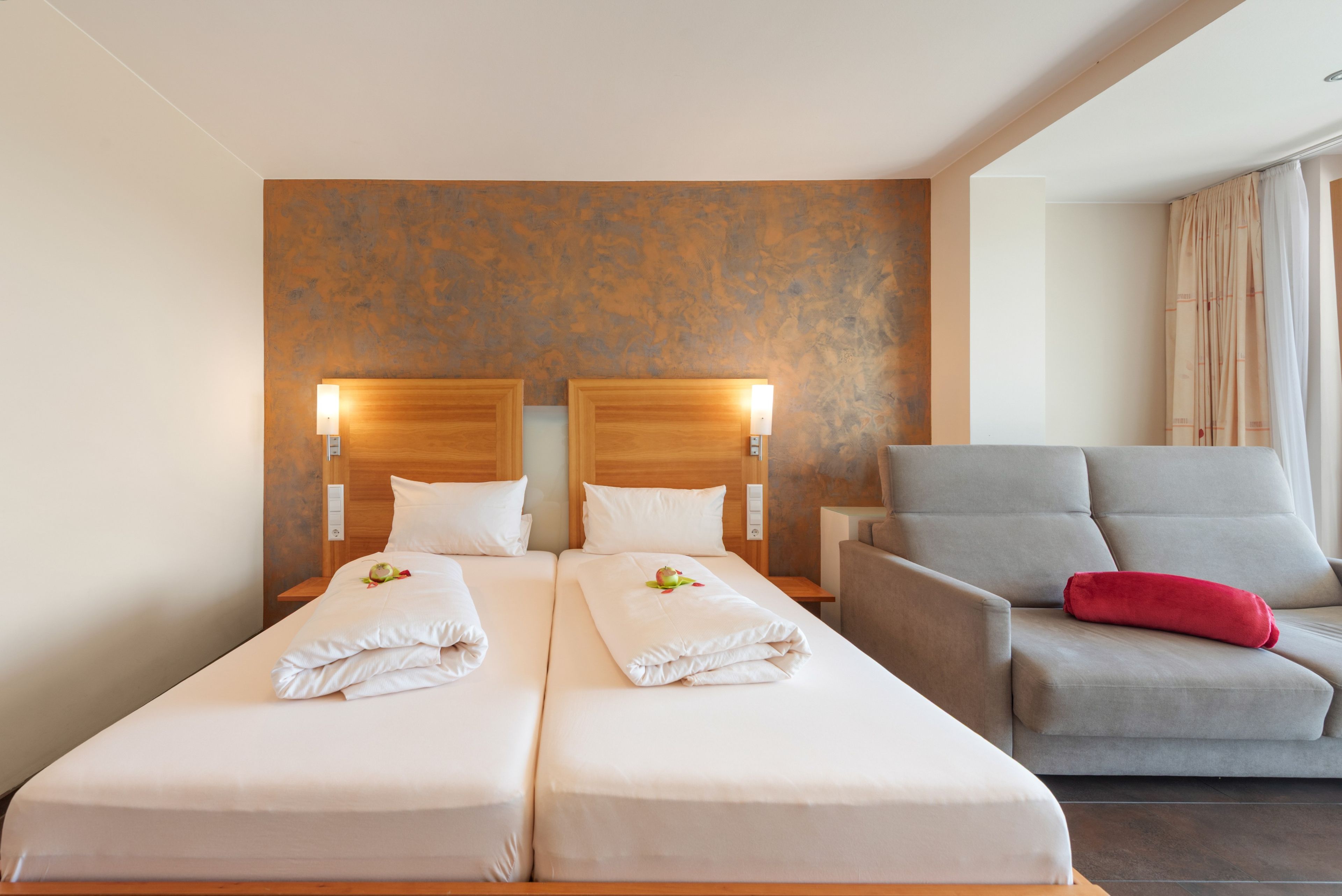 Een hotelkamer met twee bedden, een grijze fauteuil en een rood kussen.