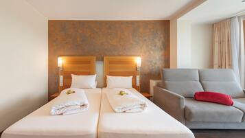 Een hotelkamer met twee bedden, een grijze fauteuil en een rood kussen.