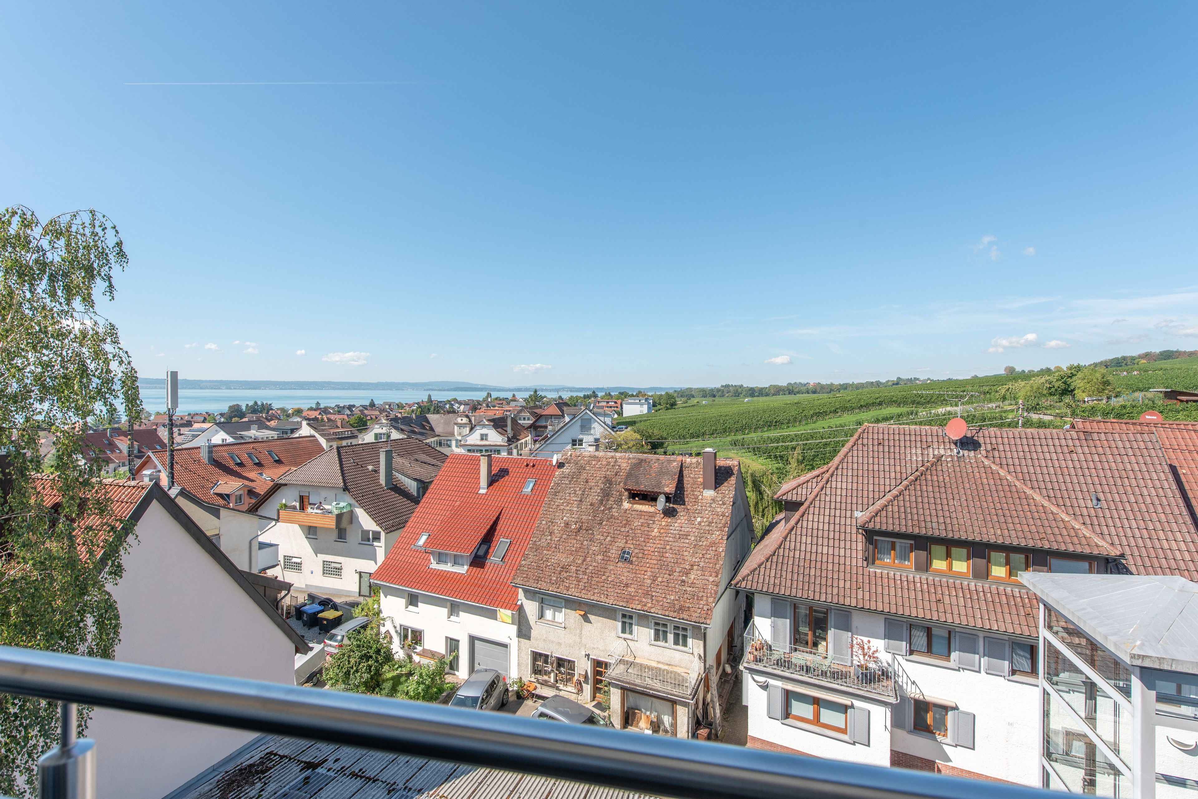 Ein Wohngebiet mit Häusern mit roten Ziegeldächern, blauem Himmel und weiter Aussicht auf ein Gewässer.