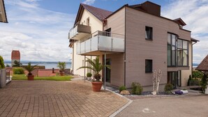 A modern two-story house with a balcony, a paved driveway, and a view of the sea. - Comfort Room with Side Lake View, Balcony and Wi-Fi (Hagnau am Bodensee)