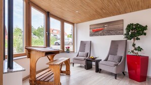 A modern living room with a wooden table, two armchairs, a red accent piece, and a view of the outdoors. - Comfort Room with Side Lake View, Balcony and Wi-Fi (Hagnau am Bodensee)