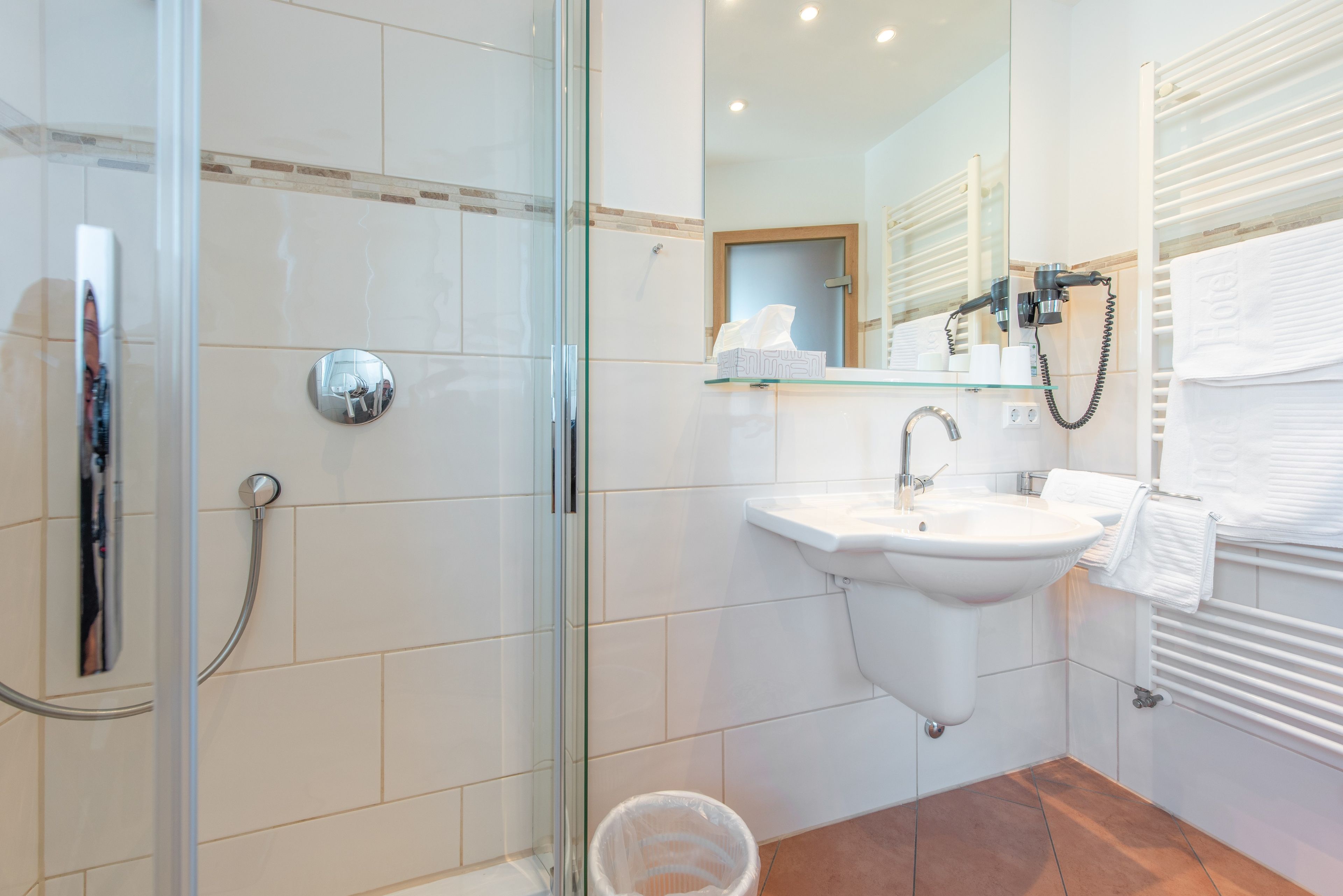 A modern bathroom with a glass shower enclosure, a white sink, and a towel rack.