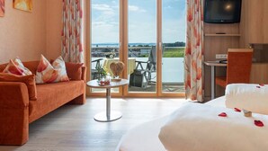 A hotel room with a sofa, a bed, a TV, and a balcony with a view of the water. - Comfort Room with Side Lake View, Balcony and Wi-Fi (Hagnau am Bodensee)