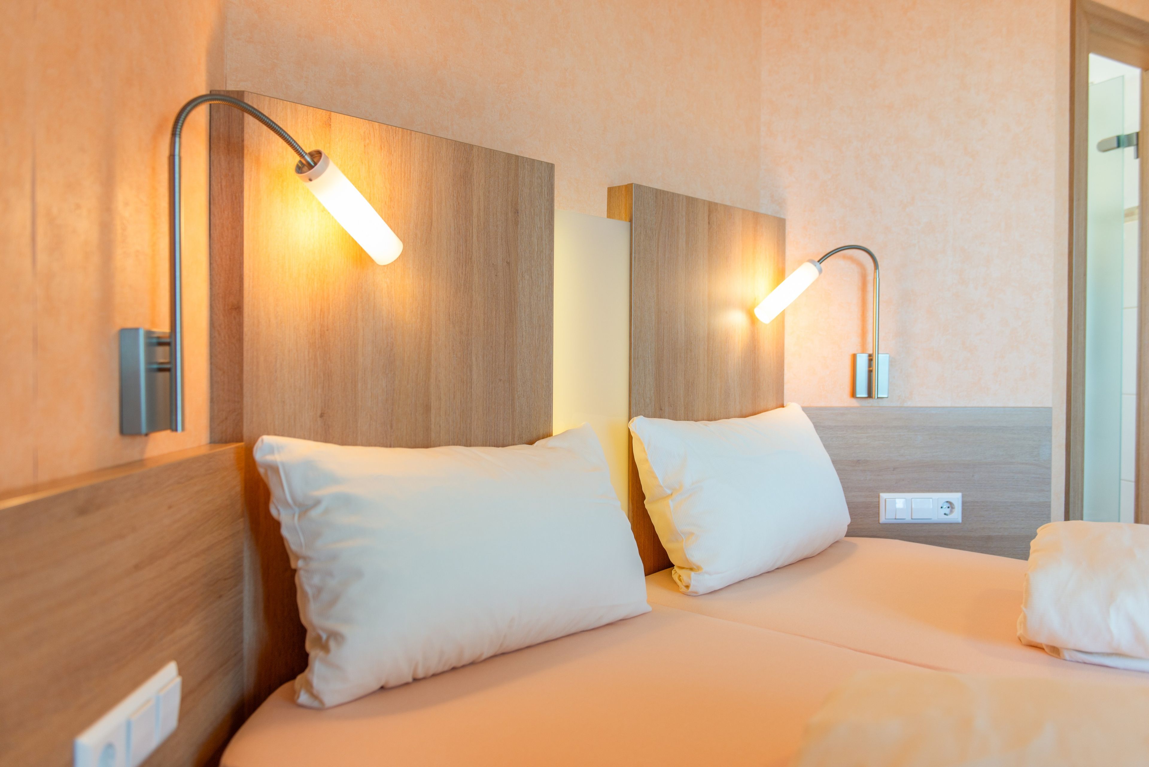 Ein Hotelzimmer mit einem hölzernen Kopfteil, zwei Nachttischlampen und einem Bett mit weißer Bettwäsche.