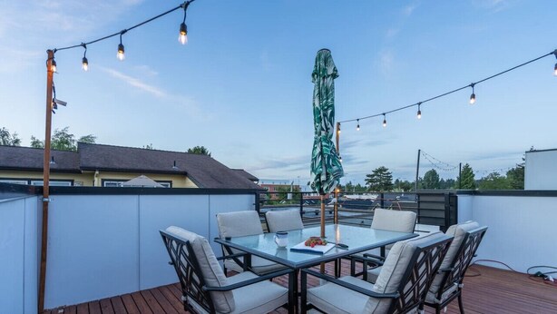 A rooftop patio with a glass table and chairs, string lights, and a large umbrella. - Rooftop Vibes!  Greenlake UW Near Down Town (Seattle)