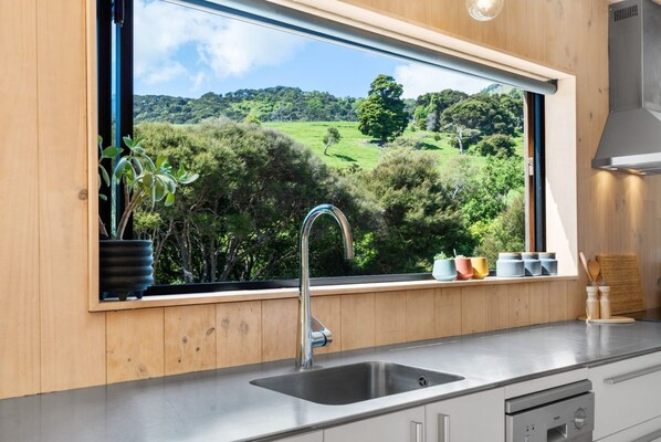 A kitchen with a large window offering a view of a green landscape. - Bellbird Bach - Akaroa (Akaroa)