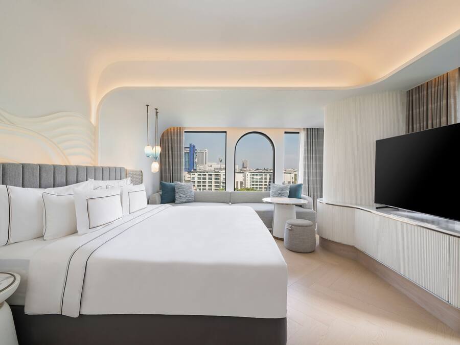 A modern hotel room with a large bed, a flat-screen TV, a city view, and a small side table.