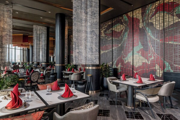 Un restaurante moderno con mesas altas, servilletas rojas y una amplia pantalla decorativa.