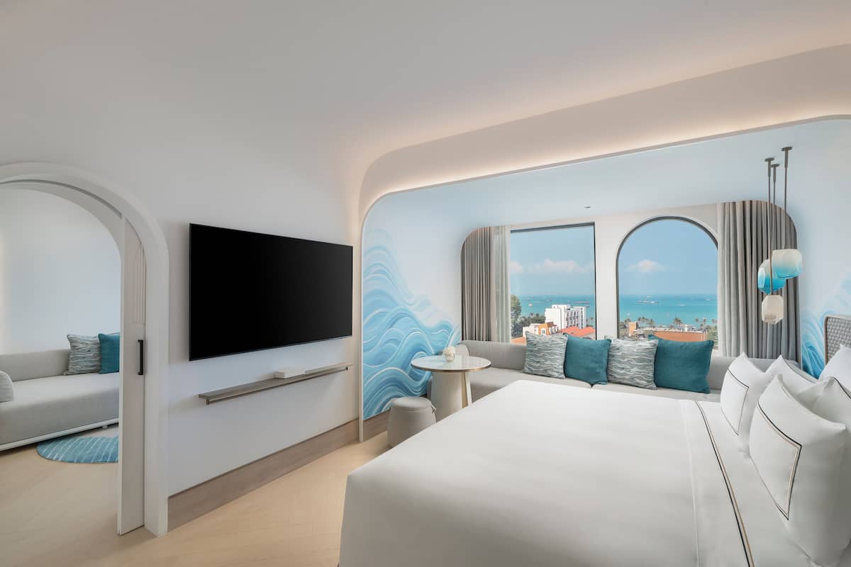 Ein modernes Hotelzimmer mit einem großen Bett, einer Couch, einem Fernseher und Blick auf die Stadt und das Meer.