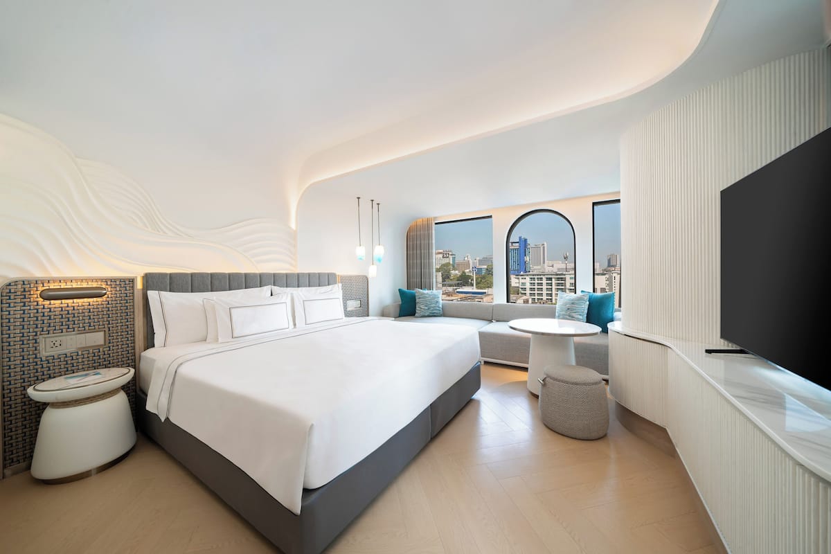 Ein modernes Hotelzimmer mit einem großen Bett, einer Sitzecke, einem Fernseher und Blick auf die Stadt.