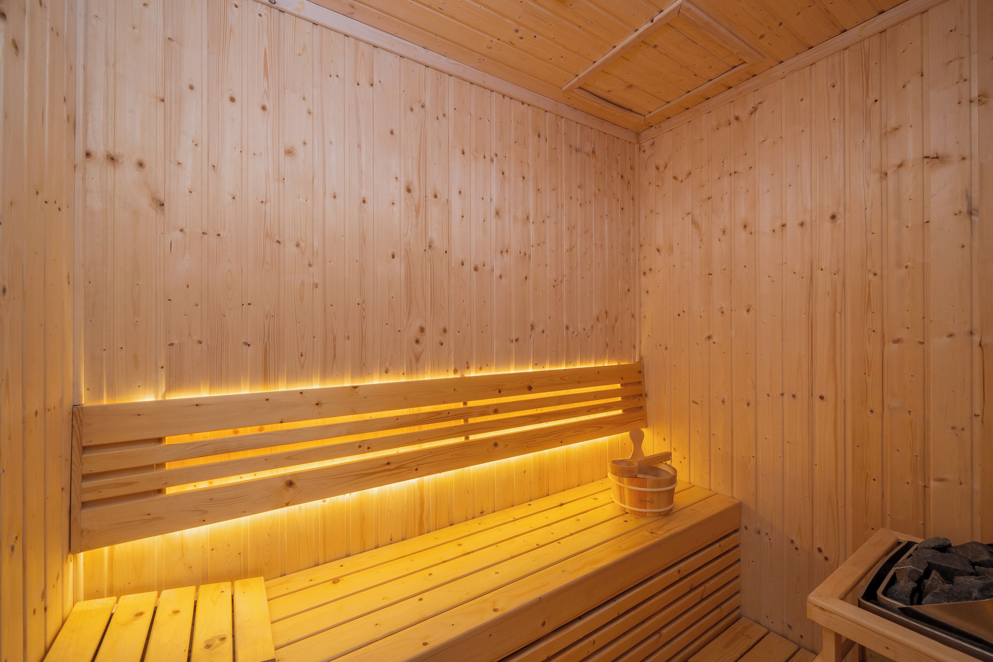 Una sauna de madera con bancos y un asiento con un cubo.