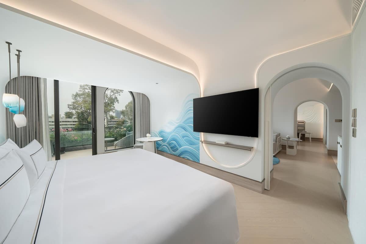 Ein modernes Hotelzimmer mit einem großen Bett, einem wandmontierten Flachbildfernseher und einem Balkon mit Stadtblick.