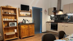 A compact kitchen with wooden cabinets, a microwave, and a dining area with a table set for two. - Pension am Lackenbach (Gaming)