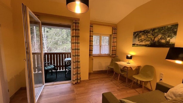 A cozy living room with a sofa, a dining table with chairs, a balcony with a table and chairs, and a painting on the wall. - Pension am Lackenbach (Gaming)