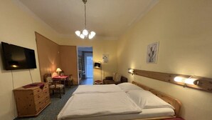 A hotel room with a large bed, wooden headboard, a flat-screen TV, a desk with a chair, and a small table with a lamp. - Pension am Lackenbach (Gaming)