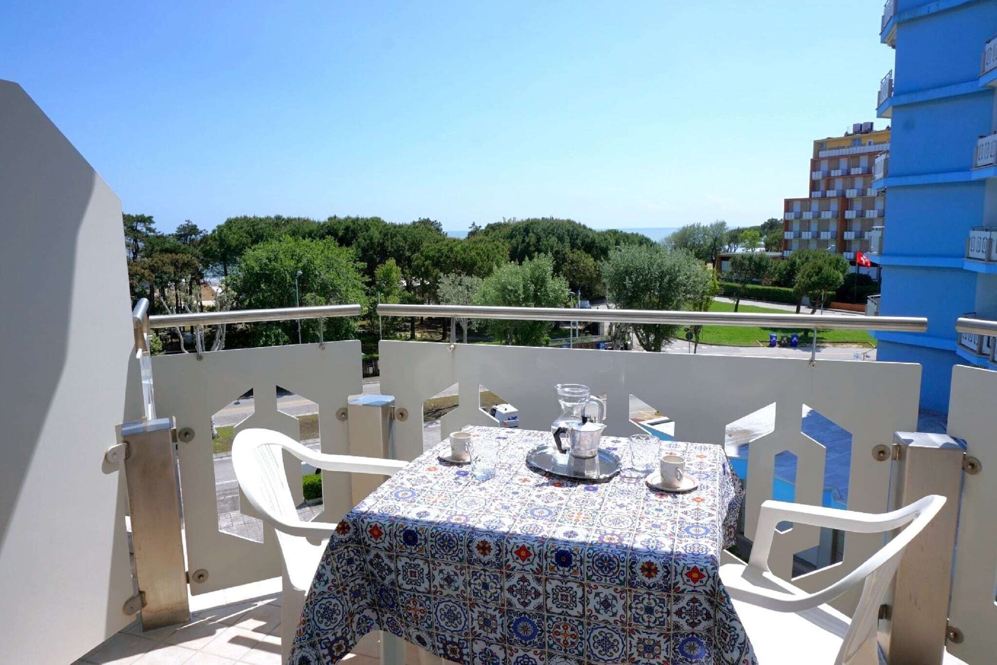 A balcony with a table set for two, overlooking a cityscape with trees and buildings.