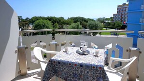 A balcony with a table set for two, overlooking a cityscape with trees and buildings.
