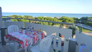 A balcony with a table set for two, overlooking a coastal view. - Apartment Porto Santa Margherita Sea Views (Porto Santa Margherita (VE))
