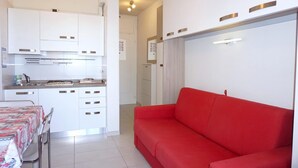 A modern kitchen with white cabinets and a red sofa in a living area. - Apartment Porto Santa Margherita Sea Views (Porto Santa Margherita (VE))