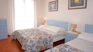 A bedroom with two beds, a nightstand, a dresser, and two framed artworks on the wall.