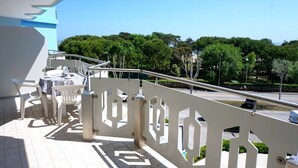 A balcony with a white railing, a table with chairs, and a view of trees and a road.