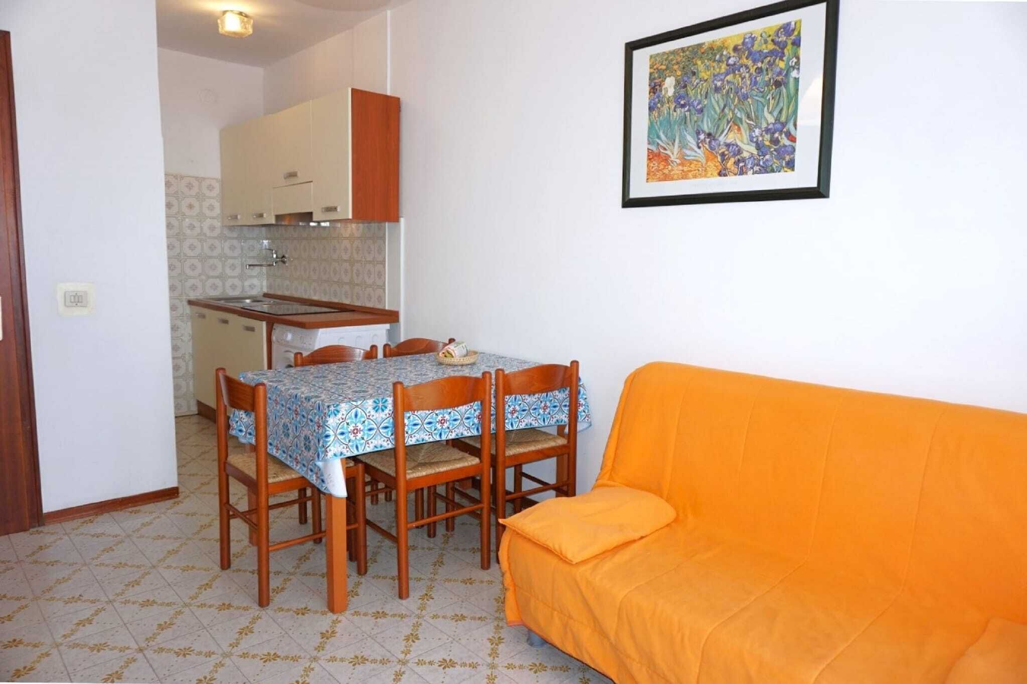 Un espai habitable compacte amb zona de menjador que inclou taula i cadires, una cuineta i un sofà taronja.