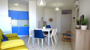Une cuisine moderne avec des meubles bleus, une table à manger avec des chaises, un canapé jaune et un meuble en bois orné de plantes.