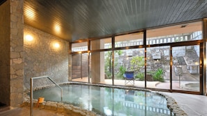A spa area with a stone wall, a glass-enclosed hot tub, and a view of the outside. - KKRDOGOYUDUKI (Matsuyama)