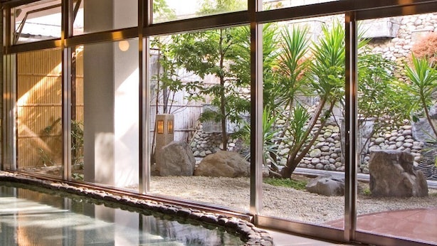 A tranquil indoor garden with a small water feature, stone walls, and a variety of plants. - KKRDOGOYUDUKI (Matsuyama)
