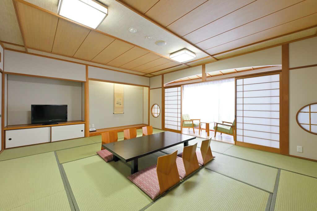 A traditional Japanese-style room with tatami flooring, a low table, and a television on a shelf.