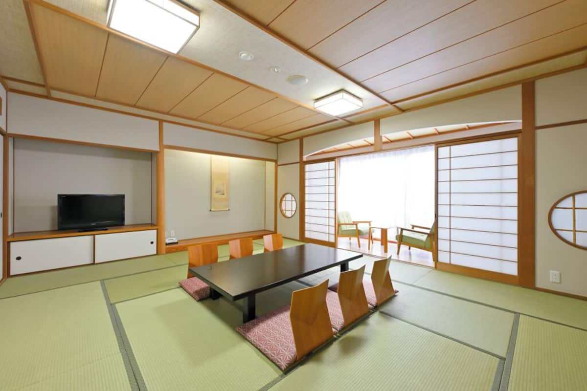 Una habitación tradicional japonesa con suelo de tatami, una mesa baja y un televisor sobre una estantería.
