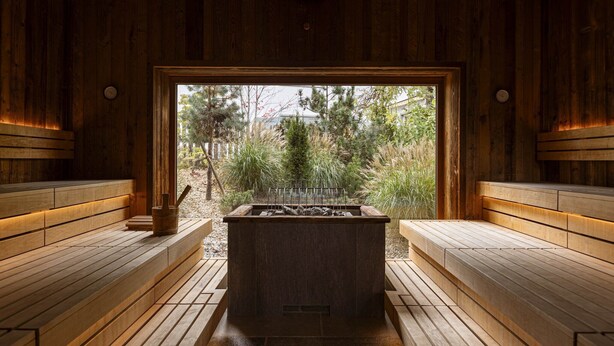 Una sauna con bancos de madera y una zona central de piedras para calentar, con un interior de madera y vistas a un área boscosa.