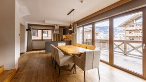Una cocina moderna con una mesa y sillas de madera, un ventanal con vistas a montañas y un balcón con barandilla de madera.