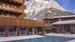 Un edificio de madera con piscina frente a un paisaje montañoso nevado.