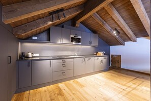 Uma cozinha moderna com armários cinza, forno de aço inoxidável e teto de madeira.