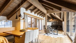 A spacious loft with a high ceiling, wooden beams, a dining area with a long table and cushioned chairs, a seating area with sofas, and large windows offering views. - Welcoming chalet with balcony (No Deposit) (Ehrwald)