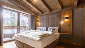 Una camera da letto con un letto grande, travi a cassetto in legno, una porta scorrevole in vetro per un balcone e due lampade fissate al muro.