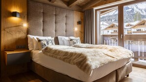 Camera da letto con un grande letto, testiera in legno e vista sulle montagne attraverso una porta di vetro.