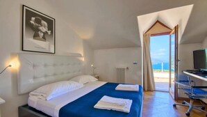 A bedroom with a bed, a desk, a chair, a radiator, and a window with a view.