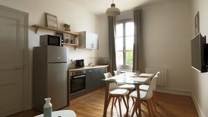 Cocina compacta equipada con refrigerador, microondas y horno. Se observa una mesa de comedor con sillas y una lámpara colgante.