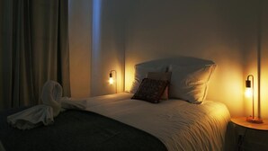 Habitación de hotel con cama, dos lámparas de noche, una mesita de noche, una bata y una cortina.