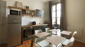 Una cocina moderna con refrigerador, microondas y horno, y un comedor con mesa de vidrio y sillas blancas.