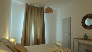A hotel room with a bed, a bedside lamp, a mirror, a dresser, and a window with curtains.