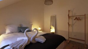A bedroom with a bed, a hanging light fixture, a mirror, and a coat rack. - Le Rabelaisien, La Belle Tourangelle (Tours)