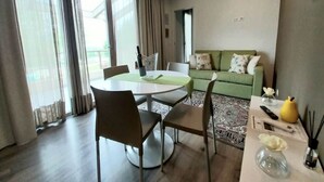 A dining area with a round table and chairs, a green sofa, and a small table with a vase and a bottle. - Apartment in Iseo with Pool (Cazzago San Martino)