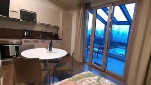 A room with a bed, a round dining table, chairs, a kitchen area, and a large sliding glass door leading to an outdoor area. - Apartment in Iseo with Pool (Cazzago San Martino)
