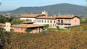 A large building with multiple floors and a balcony, surrounded by vineyards and hills in the background. - Apartment in Iseo with Pool (Cazzago San Martino)