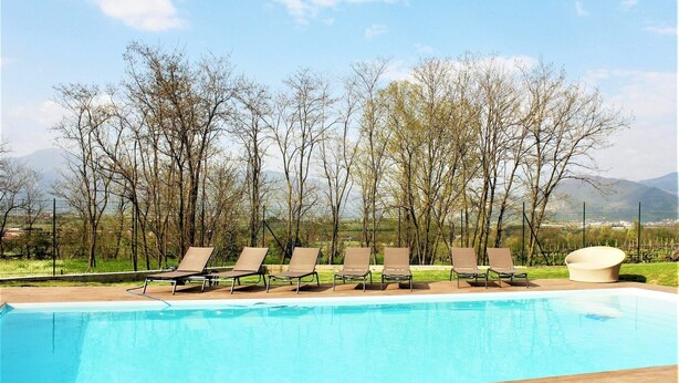 A swimming pool with lounge chairs and a modern seating area, surrounded by trees and mountains in the background. - Apartment in Iseo with Pool (Cazzago San Martino)