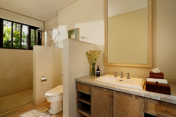 Un baño moderno con inodoro, ducha y lavamanos. Un espejo grande está sobre el lavamanos y hay un florero con flores en la encimera.